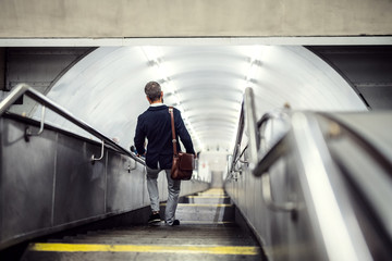 Rear view of hipster businessman walking down the stairs in subway, travelling to work.