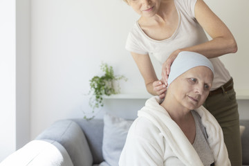 Daughter helping sick mother with headscarf after chemotherapy