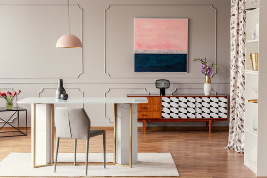 Real photo of a dining room interior with a table, pink painting and vintage cabinet