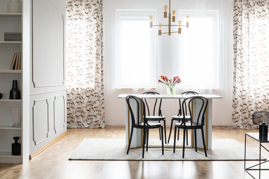 Real photo of a cozy dining room interior with patterned curtains, table, chairs and wall molding