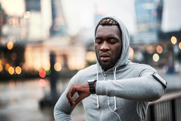 Black man runner with smartphone in an armband on the bridge in London, resting.