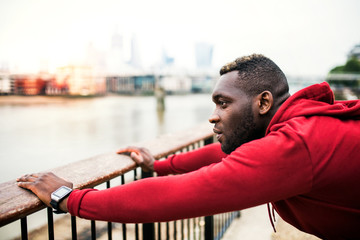 Young sporty black man runner on the bridge outside in a city, stretching.