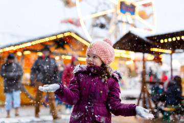 Little cute kid girl having fun on traditional Christmas market during strong snowfall. Happy child...