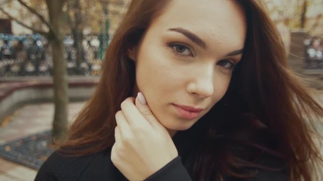 Beautiful woman posing in street. Portrait of glamorous young girl walking outdoors. Close up face of elegant woman with beautiful eyes and lips. Pretty fashion model looking at camera