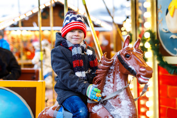 Adorable little kid boy riding on a carousel horse at Christmas funfair or market, outdoors.