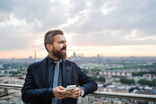 A portrait of businessman with smartphone standing against London view panorama.