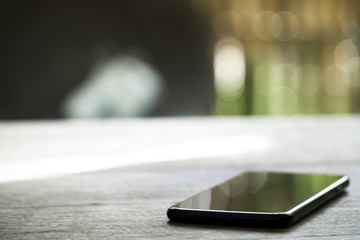 black charging mobile phone on the wooden table on blured nature background.