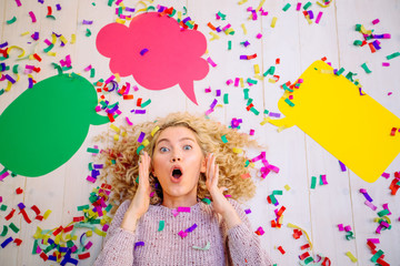 Obraz na płótnie Canvas The new idea. Curly blond excited girl lying with colorful confetti at the head of the new ideas in the form of empty colorful bubbles for text, on white floor background.