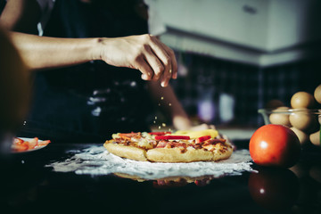 Close up of woman hand putting oregano over tomato and mozzarella on a pizza. Cooking concept - obrazy, fototapety, plakaty