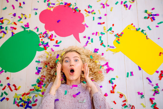 The new idea. Curly blond excited girl lying with colorful confetti at the head of the new ideas in the form of empty colorful bubbles for text, on white floor background.