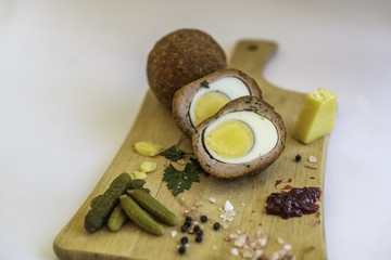 Scotch Eggs on wooden platter with traditional English Cheddar Cheese, Gherkins, condiments and garnish. 