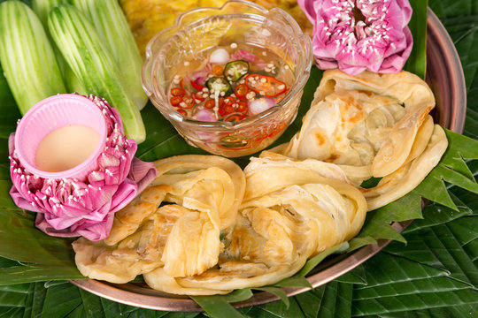 Fish Roti Mataba (filled roti) served with a sweet chili vinegar dip and cucumber salad in a white plate placed on wooden background. Thai Desserts
