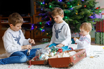 Two little kid boys and adorable baby girl decorating Christmas tree with old vintage toys and balls.