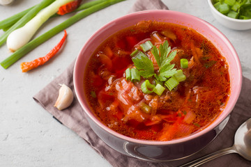 Borsch, beetroot soup in a wooden bowl with fresh herbs on a light background.