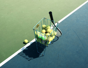 Tennis court with tennis balls in tennis ball basket stand with natural shadows. Intentionally shot in surreal tone.
