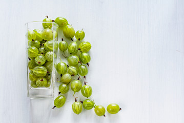 Green fresh gooseberries in a glass on white wooden background. Flat layout. Copy space