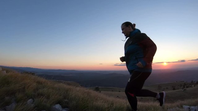 Woman running up the grassy slope on the mountain at sunset