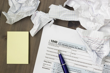 A photo from above of USA IRS tax form 1040, yellow notes, crumpled paper sheets and a pen on the wooden table. Top veiw, selective soft focus. - 225340880