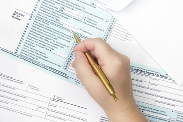 A photo from above of a Tax Form 1040. A woman signing or filling the form. The 1040 income tax form. Top veiw, selective soft focus on the hand.