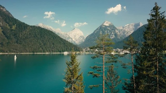 Aerial View on the mountain lake with yachts in morning time in summer sunny day under sun light. Beautiful mountains landscape view. Drone 4K Video.