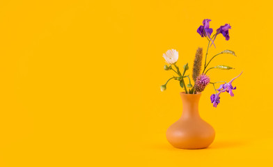 Beautiful wild flowers bouquet, brown clay vase on yellow background. Summer time floristic still life photo. Shallow depth of field, copy space.