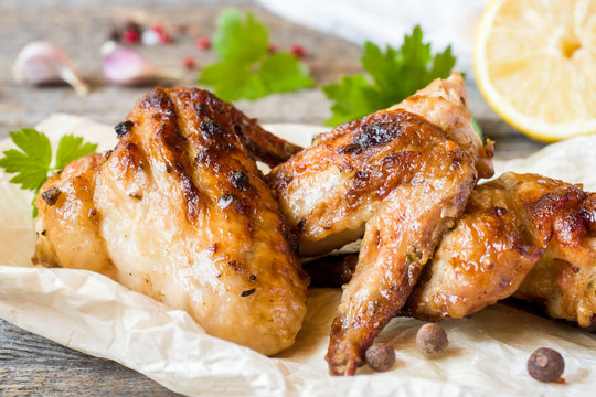 Chicken wings baked on grill with fresh herbs, lemon on wooden background.