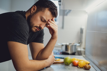 Man with headache leaning on the kitchen countertop