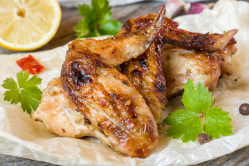 Chicken wings baked on grill with fresh herbs, lemon on wooden background.