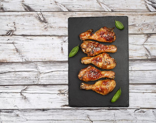 Roasted chicken drumsticks with sesame on black slate on light wooden background