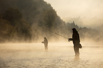 Mannen vissen in de rivier met vlieghengel tijdens de zomerochtend.