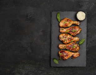 Roasted chicken drumsticks with sesame on slate on black background