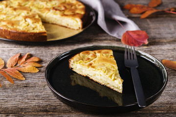 Sweet Italian zucchini pie or clafoutis cut on a plate on old rustic wooden table with yellow and red leaves. Autumn treat. Selective focus