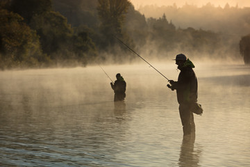 Mannen vissen in de rivier met vlieghengel tijdens de zomerochtend.