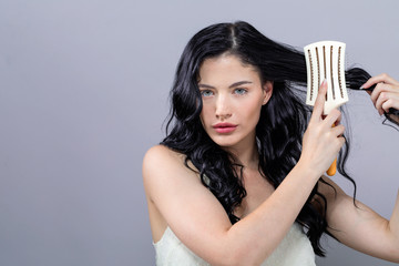 Beautiful young woman holding a hairbrush on a gray background