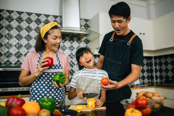 Cute girl help her parents are cutting vegetables and smiling while cooking together in kitchen at home.