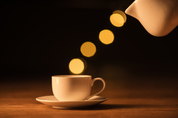 close up view of white jug, cup of coffee and bokeh lights on black backdrop