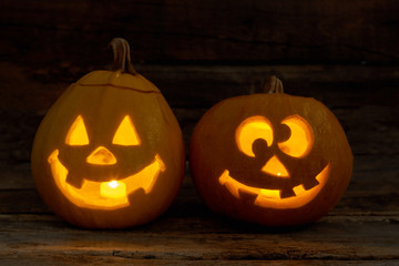Two funny pumpkins with glowing candles. Halloween pumpkin Jack-O-Lantern with happy face on dark background. Happy Halloween Day.