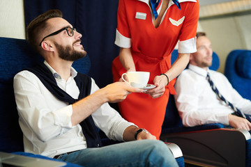 Portrait of handsome businessman smiling while taking coffee served by flight attendant in first class, copy space - obrazy, fototapety, plakaty