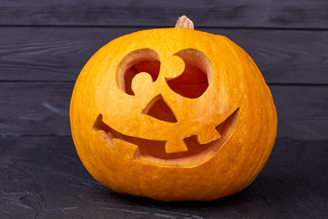 Halloween pumpkin with funny face on black background. Traditional Jack-O-Lantern on dark surface. Symbol of autumn holiday.