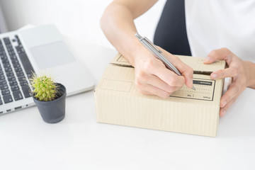 hands of woman writing on cardboard box at table, working at home concept, online marketing packaging box and delivery.