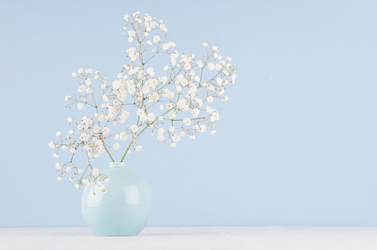 Fototapeta Spring bouquet of white small fluffy flowers in blue smooth circle ceramic vase on soft white wood table and pastel blue wall.