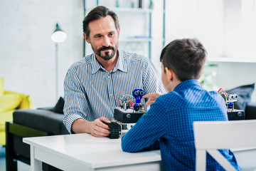 Pleasant helpful father enjoying robotic engineering with his son