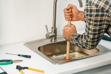 cropped image of plumber using plunger and cleaning sink in kitchen
