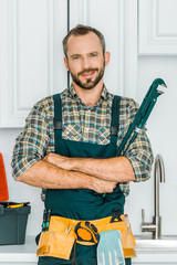 handsome plumber holding monkey wrench and looking at camera in kitchen