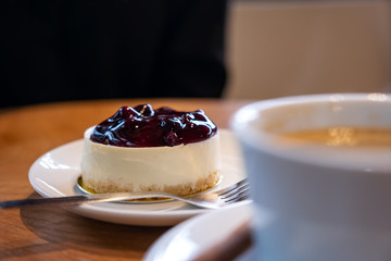 A piece of blueberry cheese cake and  coffee cup on wooden table