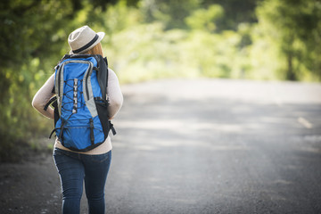 Rear of young woman backpacker walking on forest path and viewing nature around.