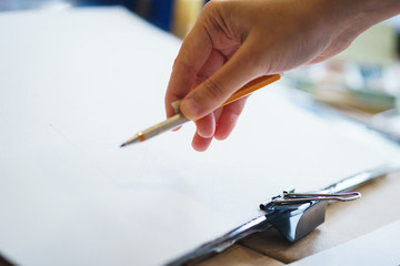 Artist with a pencil close-up while drawing a sketch on clean paper.