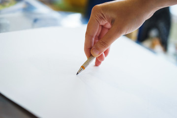 Artist with a pencil close-up while drawing a sketch on clean paper.