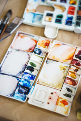Palette with watercolors in different colors. Various brushes and pencils for drawing prepared by the artist for work.