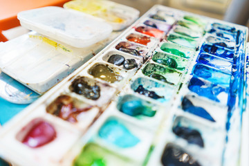 Palette with watercolors in different colors. Various brushes and pencils for drawing prepared by the artist for work.